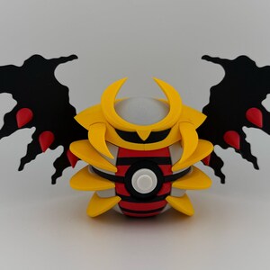 May include: A stylized, three-dimensional figure with a yellow helmet and body, black wings with red accents, and a red and black striped midsection. The figure has a white button-like detail in the center.