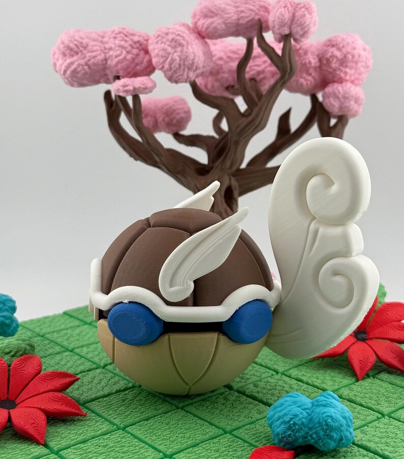 Pode incluir: Uma escultura artesanal e caprichosa com um personagem castanho, bege e azul com detalhes brancos e um grande elemento branco rodopiante. Uma &aacute;rvore castanha com flores cor-de-rosa ao fundo. A escultura assenta numa superf&iacute;cie verde texturizada com detalhes florais vermelhos e azuis.