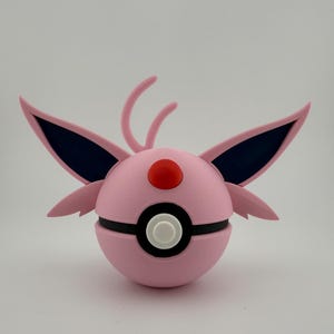 May include: A pink and black spherical object with wing-like appendages and a red button on top. The object has a white button in the center and is likely a decorative item or toy.