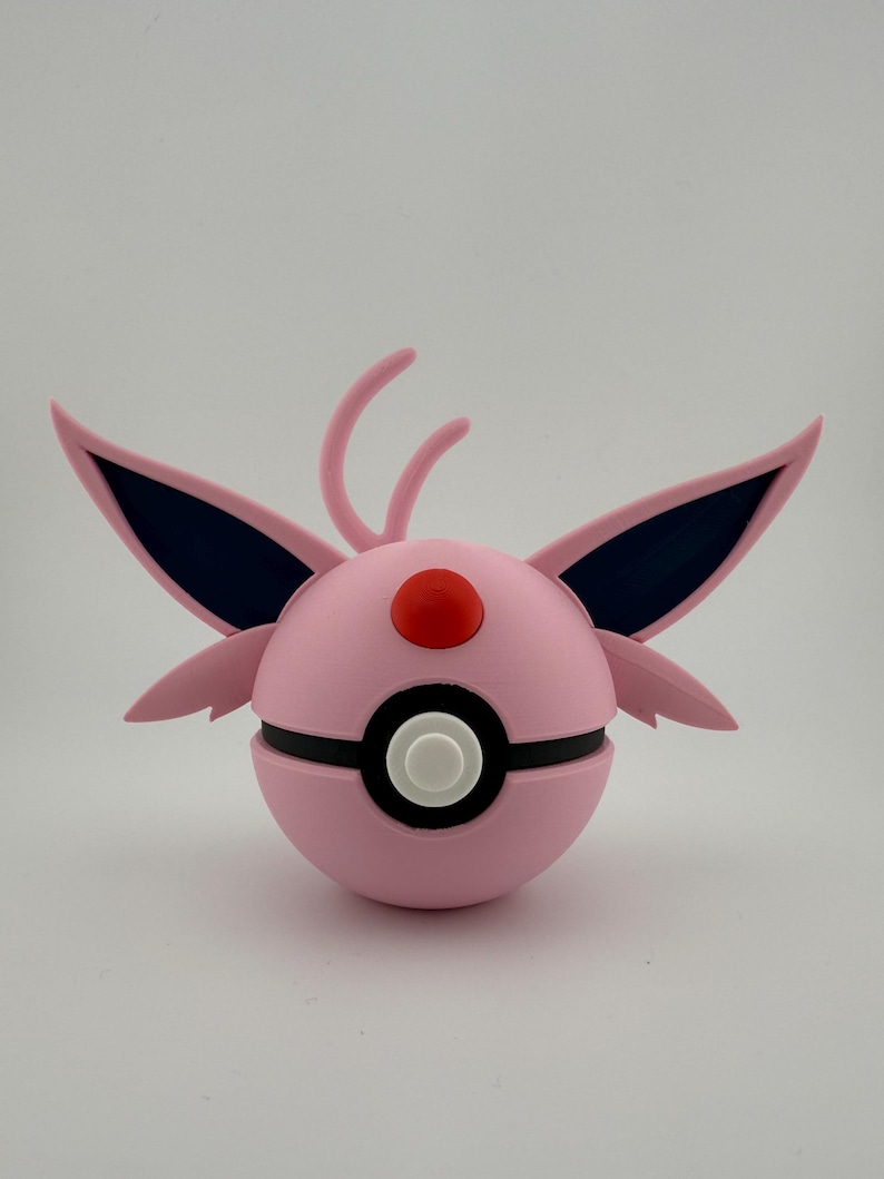 May include: A pink and black spherical object with wing-like appendages and a red button on top. The object has a white button in the center and is likely a decorative item or toy.