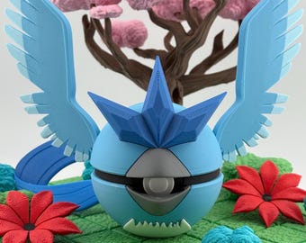 Op de afbeelding: Een lichtblauwe, bolvormige figuur met blauwe vleugels en een stervormige hoofdtooi. Het beeldje staat op een groen platform met rode bloemen en een roze boom op de achtergrond. Het algehele ontwerp is grillig en gedetailleerd.