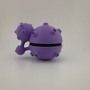 May include: A unique, purple, spherical object with a black band around the middle. The object has several small, round protrusions and a smaller, connected sphere with similar features. The design is reminiscent of a stylized planet or space-themed item.