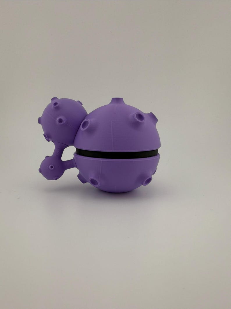 May include: A unique, purple, spherical object with a black band around the middle. The object has several small, round protrusions and a smaller, connected sphere with similar features. The design is reminiscent of a stylized planet or space-themed item.