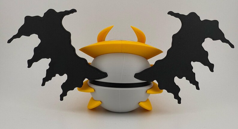 May include: A whimsical, stylized creature with a rounded, gray body, yellow accents, and large, black, wing-like appendages. The creature has a yellow hat and horns. The design is reminiscent of a cartoon character or a fantasy creature.