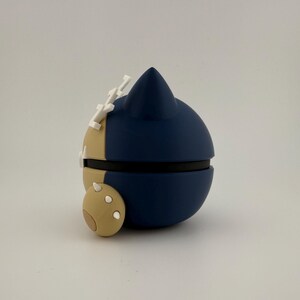 May include: A navy blue and tan spherical object with white accents. The object has a rounded shape with a pointed top and a small, circular appendage. The object is likely a decorative item or a collectible.