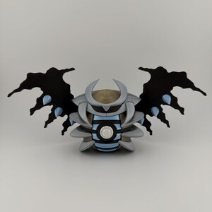 May include: A 3D-printed sculpture of a stylized creature with black wings, gray body, and blue accents. The sculpture has a circular design in the center and a horned head. The wings have a jagged edge.
