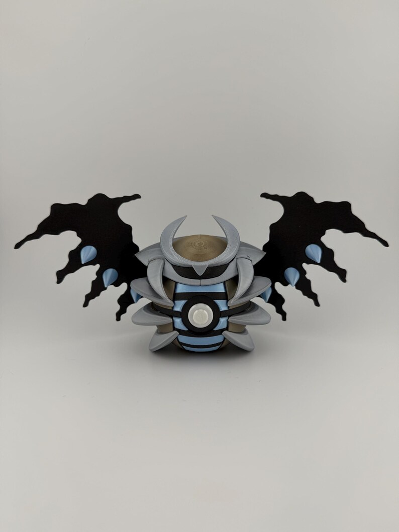 May include: A 3D-printed sculpture of a stylized creature with black wings, gray body, and blue accents. The sculpture has a circular design in the center and a horned head. The wings have a jagged edge.