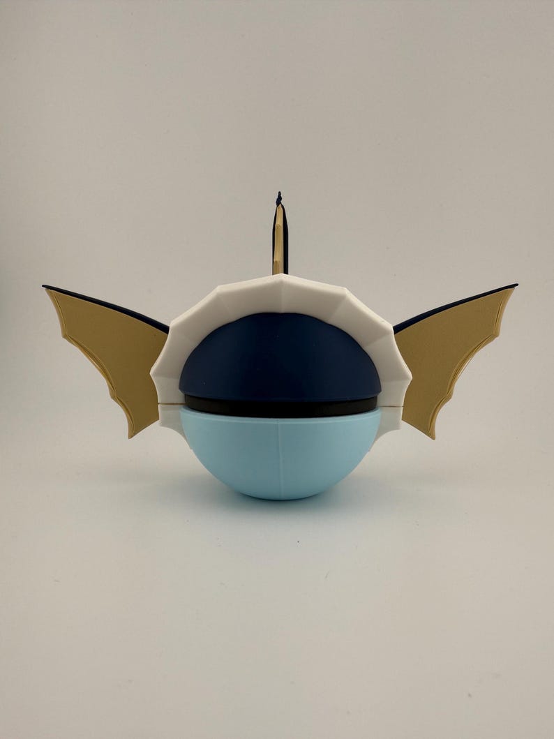 May include: A unique, stylized sculpture with a light blue, navy blue, and white color scheme. The sculpture has a rounded base, a segmented white top, and gold-colored wing-like elements on either side. A thin, black and gold element rises from the top.