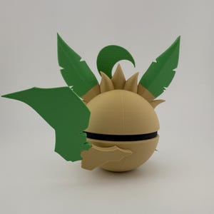May include: A 3D-printed decorative object with a spherical base in a light tan colour, accented with a black band. Green leaf-shaped elements and a curved accent are attached to the sphere, creating a stylized, plant-like design.