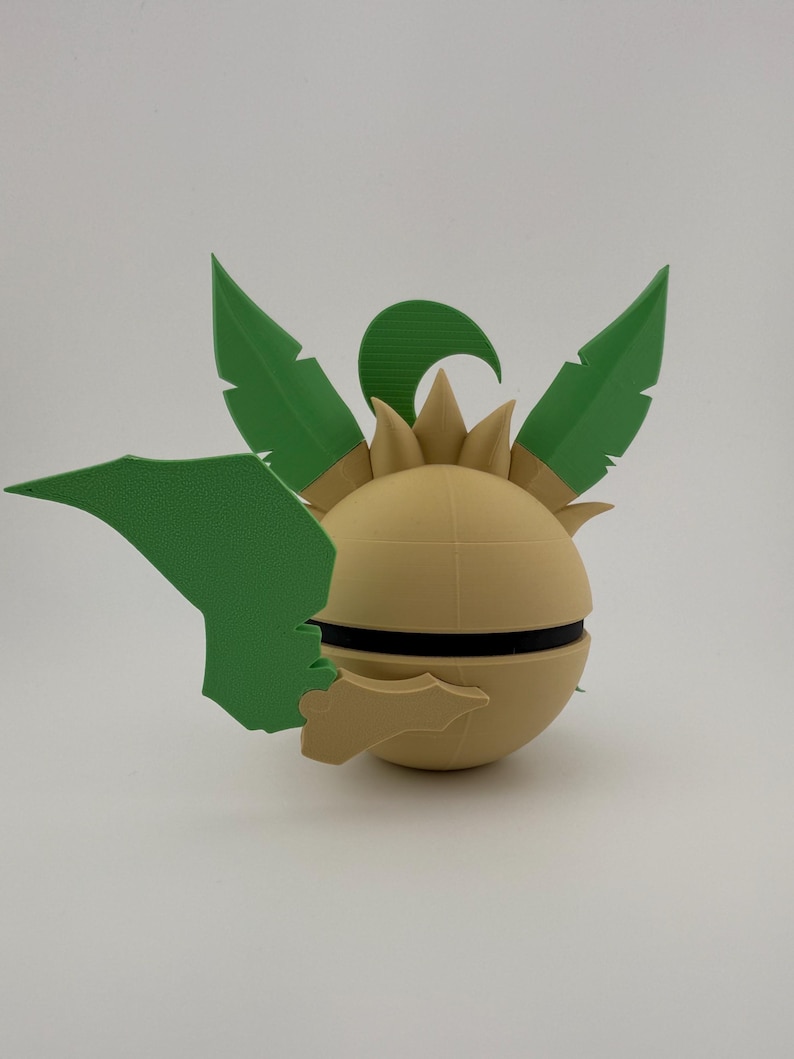 May include: A 3D-printed decorative object with a spherical base in a light tan colour, accented with a black band. Green leaf-shaped elements and a curved accent are attached to the sphere, creating a stylized, plant-like design.