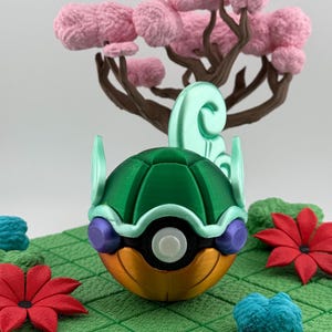 Pode incluir: Uma esfera decorativa multicolorida impressa em 3D, com uma parte superior verde, uma parte inferior laranja e um centro branco. A esfera &eacute; cercada por flores vermelhas, folhagem azul e verde e uma &aacute;rvore rosa com galhos marrons. A cena est&aacute; em uma grade verde.