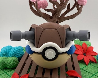 Op de afbeelding: Een gedetailleerd 3D-geprint model van een Pokémon-personage, met een bruin schild, grijze kanonnen en een crèmekleurig lichaam. Het model staat op een bruin platform met rode en blauwe bloemaccenten en een roze boom op de achtergrond.