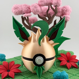 May include: A gold and green decorative sphere with a black band and white button, surrounded by green leaves and red flowers. A pink tree is in the background, set on a green grid.
