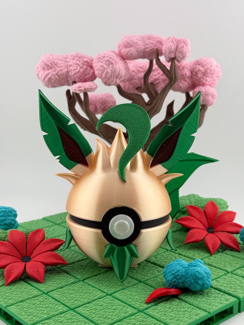 May include: A gold and green decorative sphere with a black band and white button, surrounded by green leaves and red flowers. A pink tree is in the background, set on a green grid.