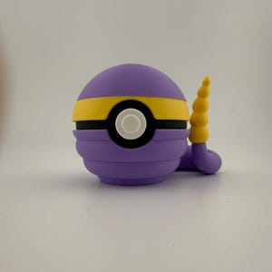 May include: A purple and yellow cartoon character with a white eye and a yellow tail. The character is round with a yellow stripe around the middle. The tail is a curved, segmented shape.