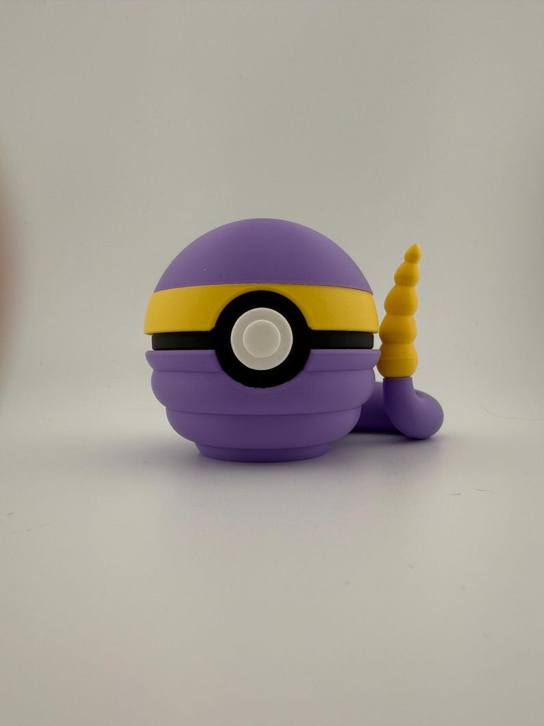 May include: A purple and yellow cartoon character with a white eye and a yellow tail. The character is round with a yellow stripe around the middle. The tail is a curved, segmented shape.