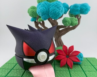 May include: A purple and black figure with red accents and a pink tongue, resembling a cartoon character, sits on a green platform. A red flower and a tree with blue and green foliage are in the background.