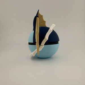 May include: A blue and black spherical object with a white and tan accent. The object has a light blue base, a dark blue top, and a white and tan fin-like structure. The object is likely a collectible or decorative item.