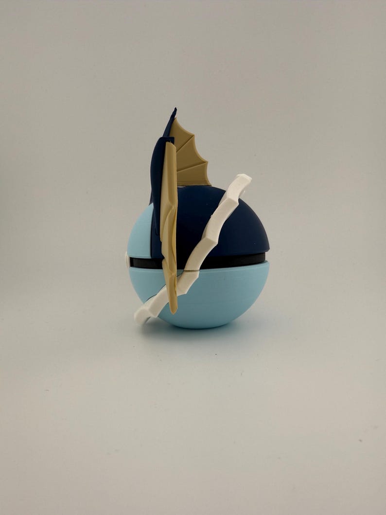 May include: A blue and black spherical object with a white and tan accent. The object has a light blue base, a dark blue top, and a white and tan fin-like structure. The object is likely a collectible or decorative item.