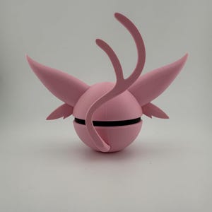 May include: A pink, spherical sculpture with wing-like projections and curved, antler-like elements. A black band encircles the sphere. The design is symmetrical and appears to be 3D-printed.