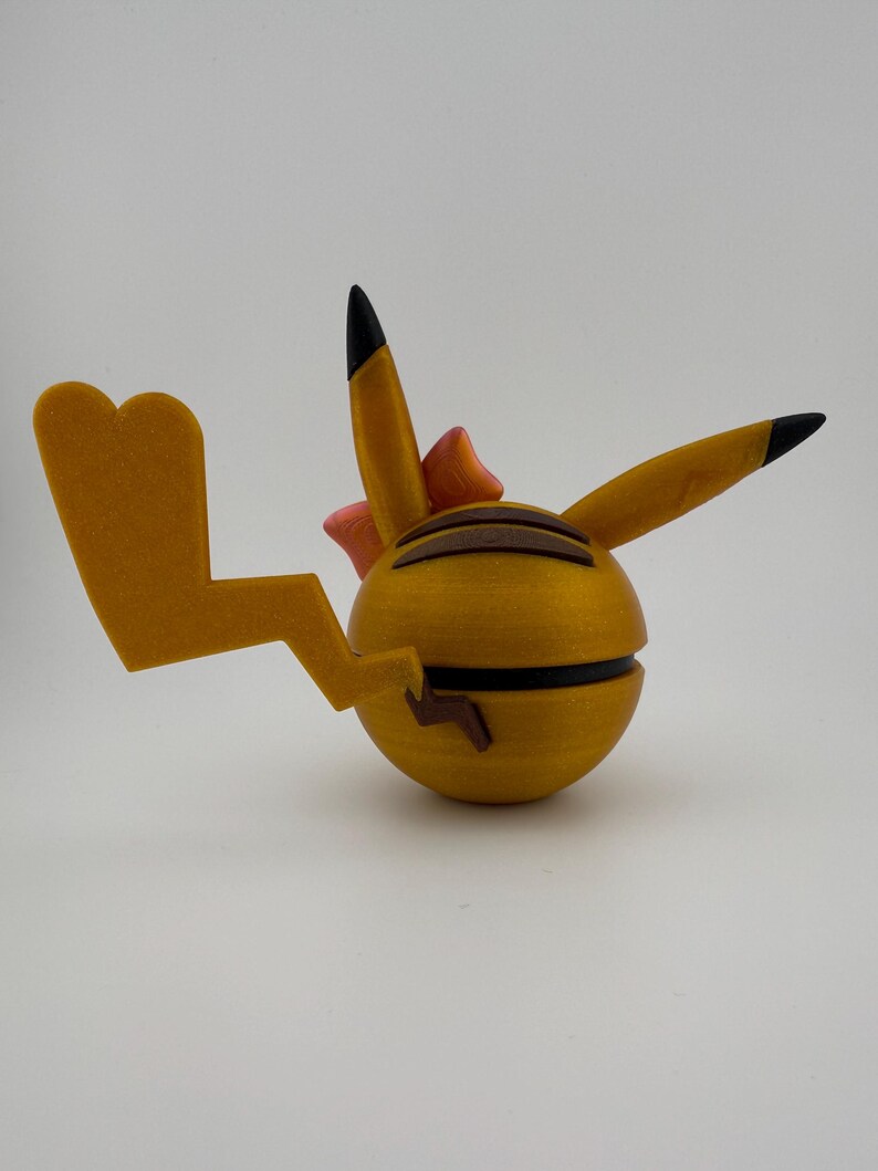 May include: A yellow, spherical figurine with black stripes and a lightning bolt tail. The figurine has two pointed ears with black tips and a small pink bow. The overall design is reminiscent of a popular cartoon character.