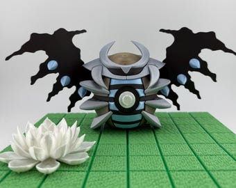 Op de afbeelding: Een gedetailleerde 3D-geprinte sculptuur van een gestileerd insectachtig wezen met zwarte vleugels en blauwe accenten. De sculptuur staat op een groene betegelde ondergrond, met een witte lotusbloem op de voorgrond.