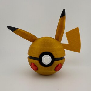May include: A golden-yellow, spherical object with black and red accents, resembling a cartoon character. The object has two pointed ears with black tips, a lightning bolt tail, and a black stripe around the middle. Two red circles are on the bottom.