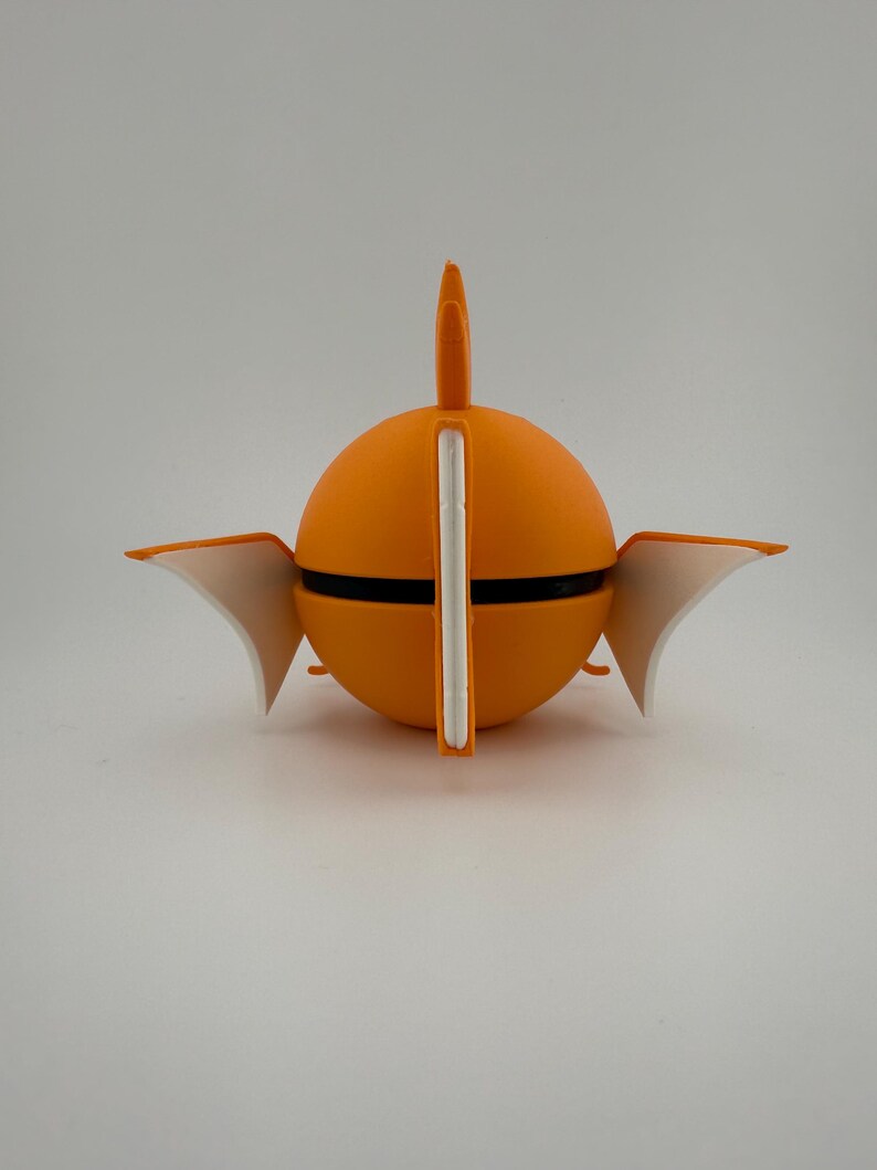 K&ouml;nnte beinhalten: Ein leuchtend orangefarbenes, kugelf&ouml;rmiges Objekt mit einem schwarzen Band, wei&szlig;en Akzenten und fl&uuml;gelf&ouml;rmigen Elementen. Ein vertikaler wei&szlig;er Balken teilt die Kugel, mit einer flossenartigen Struktur oben. Das Objekt steht vor einem schlichten wei&szlig;en Hintergrund.