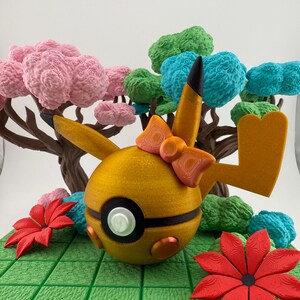 May include: A golden-yellow, spherical character with a black and white eye, orange bow, and pointed ears. The character is surrounded by a green, grid-like surface, red flowers, and colorful, textured trees with pink, green, and blue foliage.