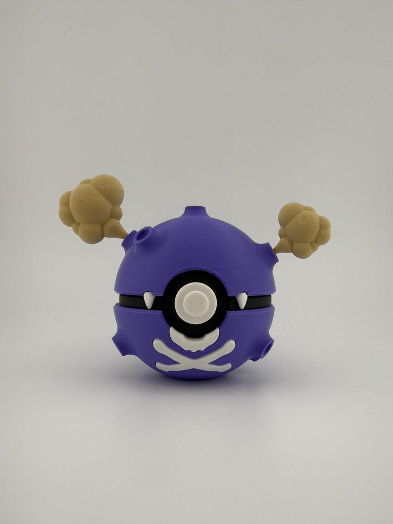 May include: A purple and white cartoon-style Poke Ball with tan smoke-like accents. The ball has a black band and a white skull and crossbones design. The design is reminiscent of a cartoon character.