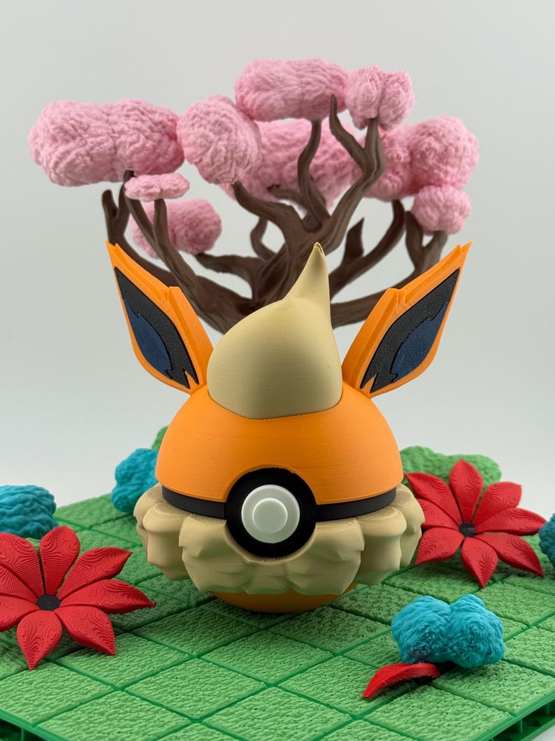 May include: A 3D-printed orange and tan figure with black accents, resembling a character from a popular animated series. It is set against a backdrop of a pink tree and green, textured ground with red and blue floral accents.