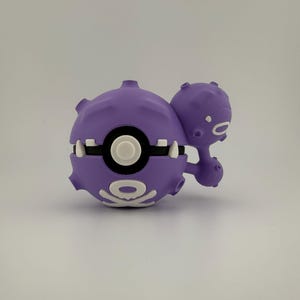 May include: A purple, stylized toy figure with a round body and a smaller, connected sphere. The figure has white accents, including a circular design and teeth-like shapes. The toy is likely a collectible or a character from a popular franchise.