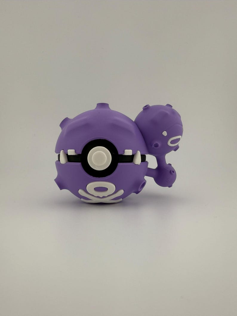May include: A purple, stylized toy figure with a round body and a smaller, connected sphere. The figure has white accents, including a circular design and teeth-like shapes. The toy is likely a collectible or a character from a popular franchise.
