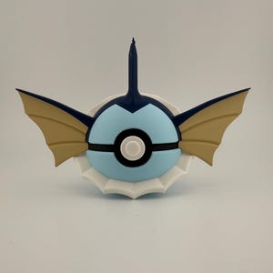 May include: A blue, tan, and white decorative item resembling a stylized creature. The item features a light blue sphere with black and white accents, tan wings, and a dark blue fin-like structure.