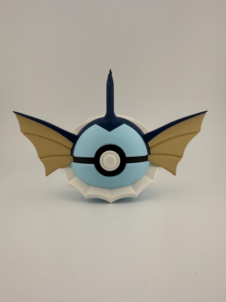 May include: A blue, tan, and white decorative item resembling a stylized creature. The item features a light blue sphere with black and white accents, tan wings, and a dark blue fin-like structure.