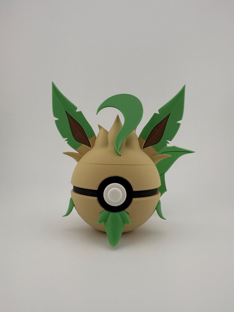 May include: A tan and green ball-shaped ornament with a black stripe and a white circle in the centre. It features green leaf-like structures and brown accents, resembling a stylized plant or creature.