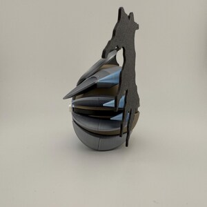 May include: A multi-layered, abstract sculpture with a rounded base and a jagged, dark gray silhouette extending upwards. The sculpture features shades of gray, blue, and brown, creating a unique, modern design. The overall shape is reminiscent of a stylized grenade.