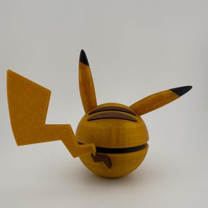 May include: A 3D-printed Pikachu figure in yellow and brown. The figure has a spherical body with a lightning bolt tail and pointed ears with black tips. The figure is a collectible item.