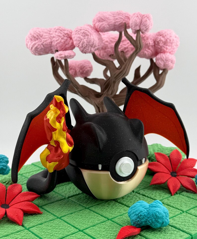 May include: A black and gold fantasy creature with red wings and a yellow and orange flame. The creature is set on a green surface with red flowers and a pink tree in the background. The scene is a whimsical, fantasy-themed design.