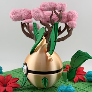 May include: A gold-coloured, spherical object with green leaf-like accents and a black stripe, set on a green grid. A pink tree with brown branches and pink fluffy foliage is in the background. Red and blue floral accents are scattered around the base.