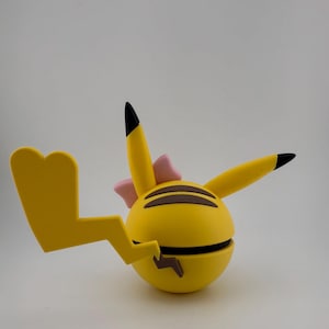 May include: A yellow, spherical toy with black stripes and a lightning bolt tail. The toy has two pointed ears with black tips and a pink bow. The toy is a stylized representation of a popular cartoon character.