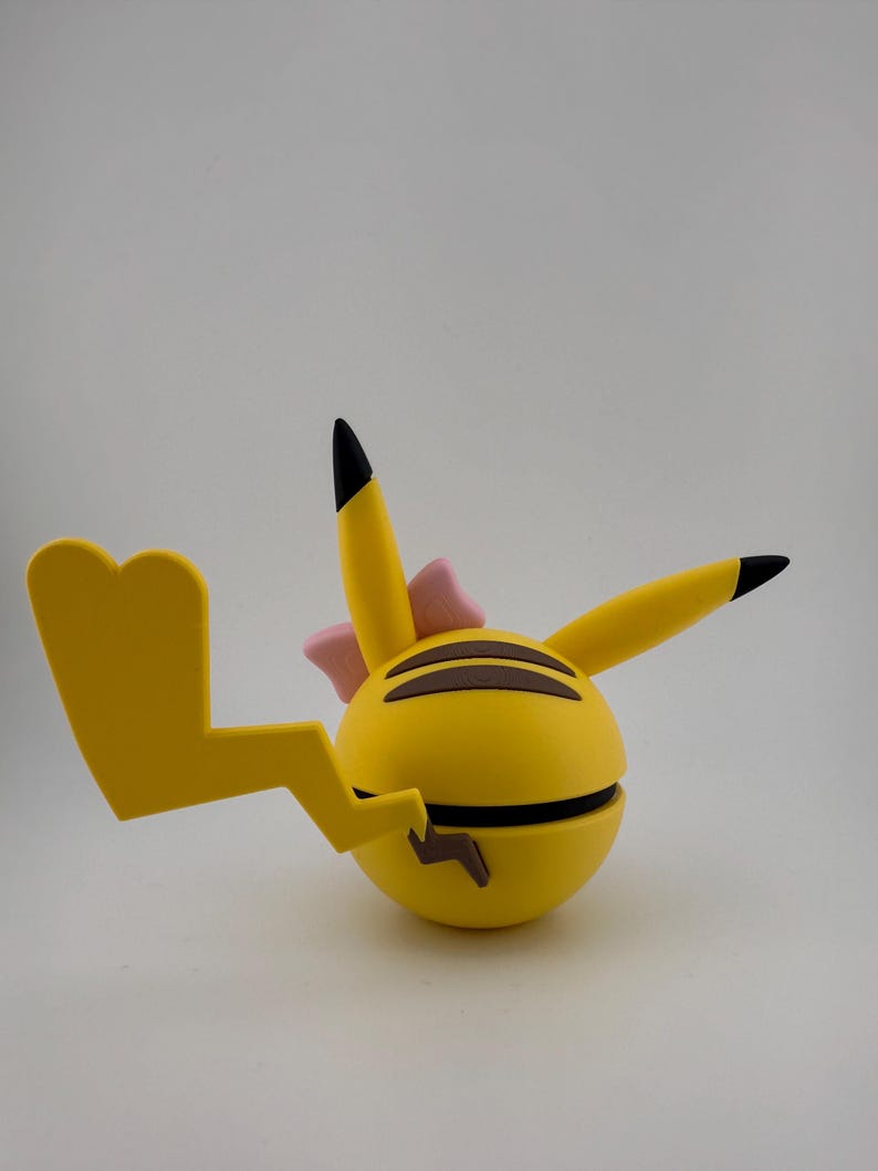 May include: A yellow, spherical toy with black stripes and a lightning bolt tail. The toy has two pointed ears with black tips and a pink bow. The toy is a stylized representation of a popular cartoon character.