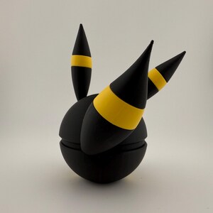 May include: A black spherical object with three black conical protrusions, each featuring a yellow band. The object is segmented, suggesting a possible opening or articulation. The design is simple and geometric.