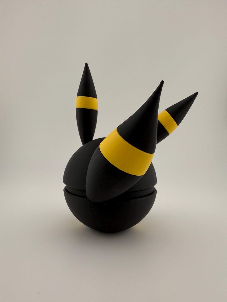 May include: A black spherical object with three black conical protrusions, each featuring a yellow band. The object is segmented, suggesting a possible opening or articulation. The design is simple and geometric.