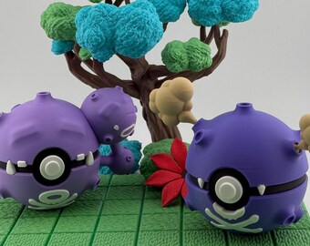 Op de afbeelding: Een diorama met twee paarse stripfiguren met witte accenten, tegen een achtergrond van een miniatuurboom met groene en blauwe bladeren. Een rood blad en een groene basis maken de scène compleet.