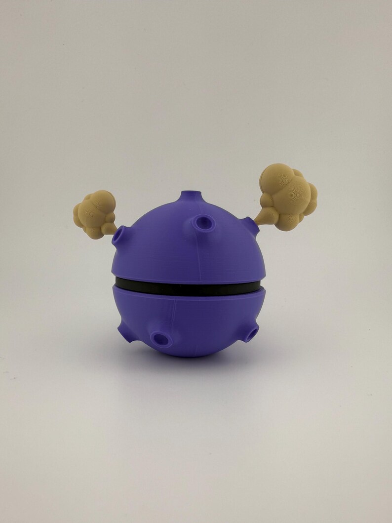 May include: A purple, spherical 3D-printed object with a black band around the middle and tan cloud-like shapes extending from the sides. The object has several circular openings and a small cylindrical protrusion on top.