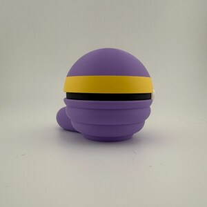 May include: A purple, spherical object with a yellow band and a small, rounded protrusion. The object has a layered design and appears to be made of a soft material. The background is plain white.