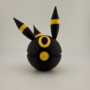 May include: A black and yellow spherical figure with three pointed projections. The figure has a circular yellow design on the front and yellow accents on the projections. The object is set against a plain white background.
