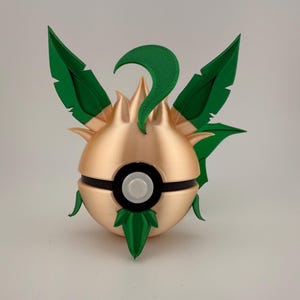May include: A 3D-printed, gold-coloured ball with green leaf-like accents and a black band. The ball has a white button in the centre and green leaves on top and bottom. The design is reminiscent of a popular video game.