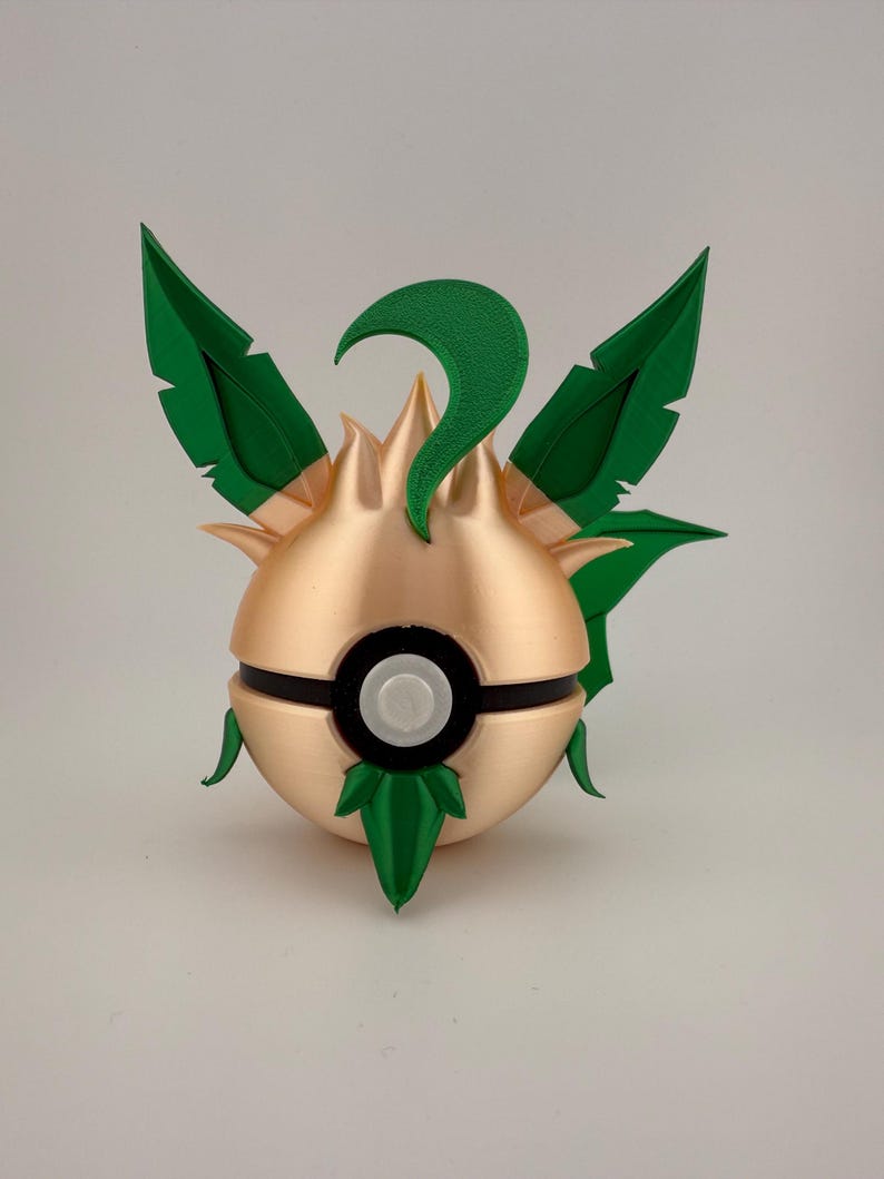 May include: A 3D-printed, gold-coloured ball with green leaf-like accents and a black band. The ball has a white button in the centre and green leaves on top and bottom. The design is reminiscent of a popular video game.